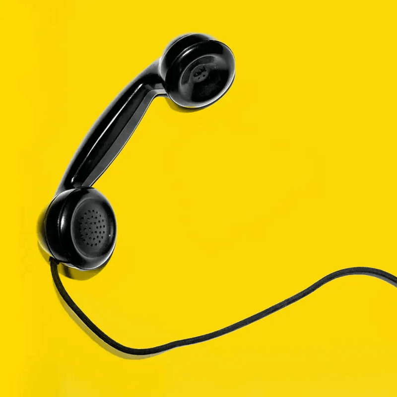 Schwarzer Telefonhörer mit Spiralkabel auf gelbem Hintergrund