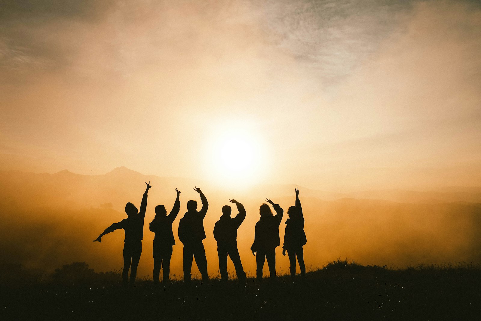 Gruppe jubelt als Silhouette vor der untergehenden Sonne