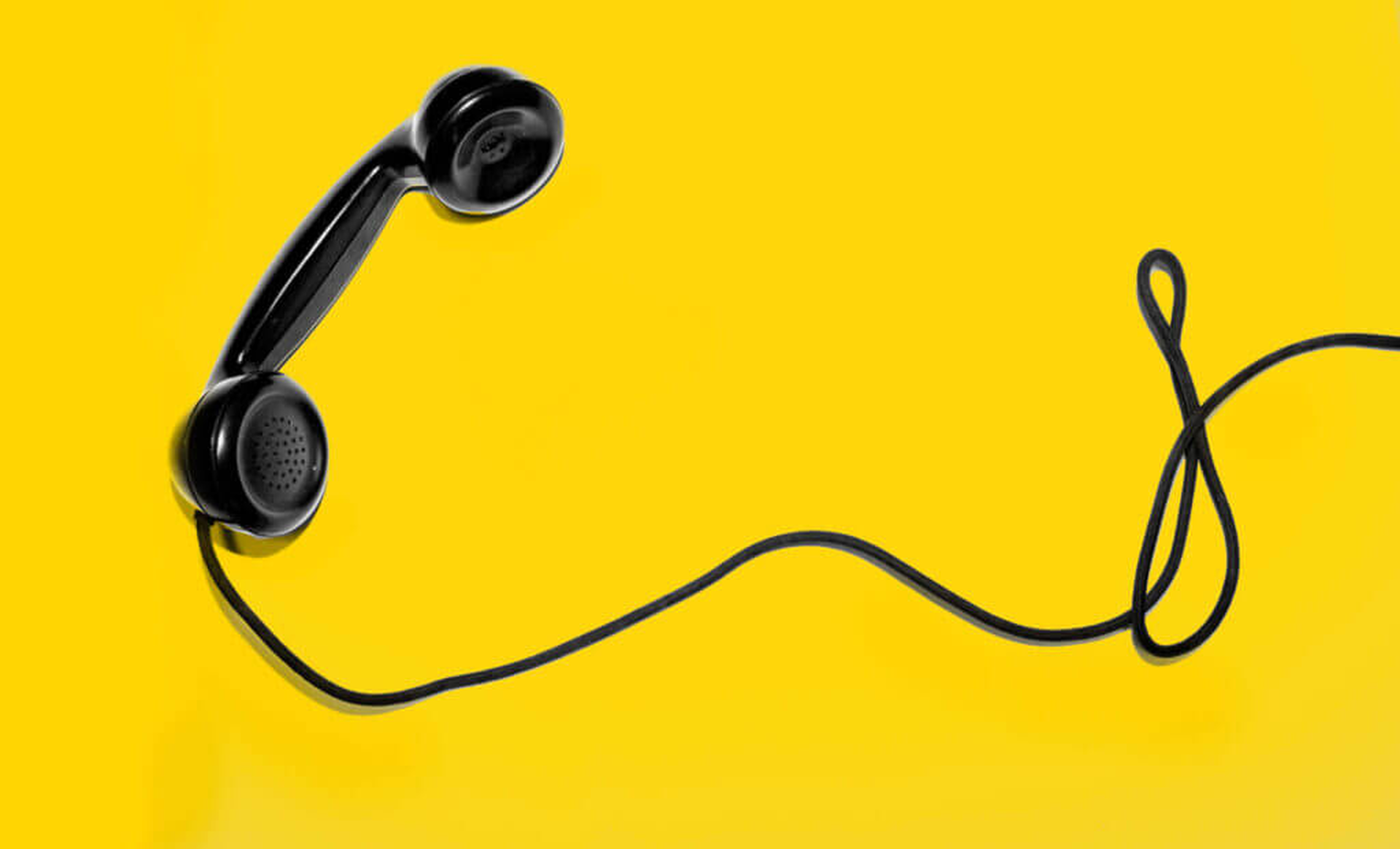Schwarzer Telefonhörer mit Spiralkabel auf gelbem Hintergrund