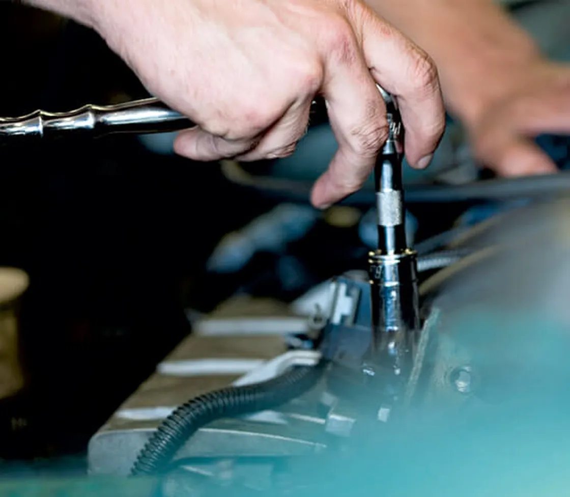 Hand zieht mit einer Ratsche eine Zündkerze am Motorblock fest