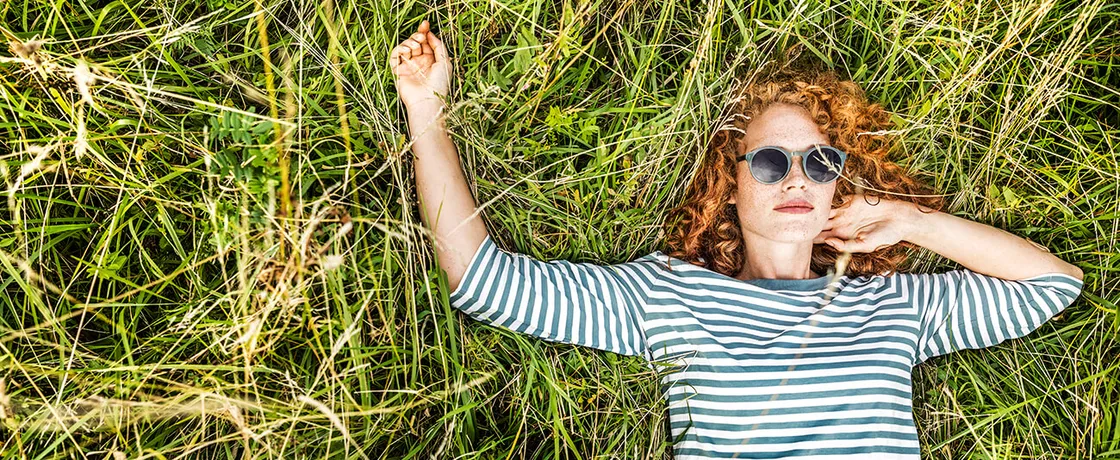 Frau liegend auf Sommerwiese mit roten Locken und Sonnenbrille