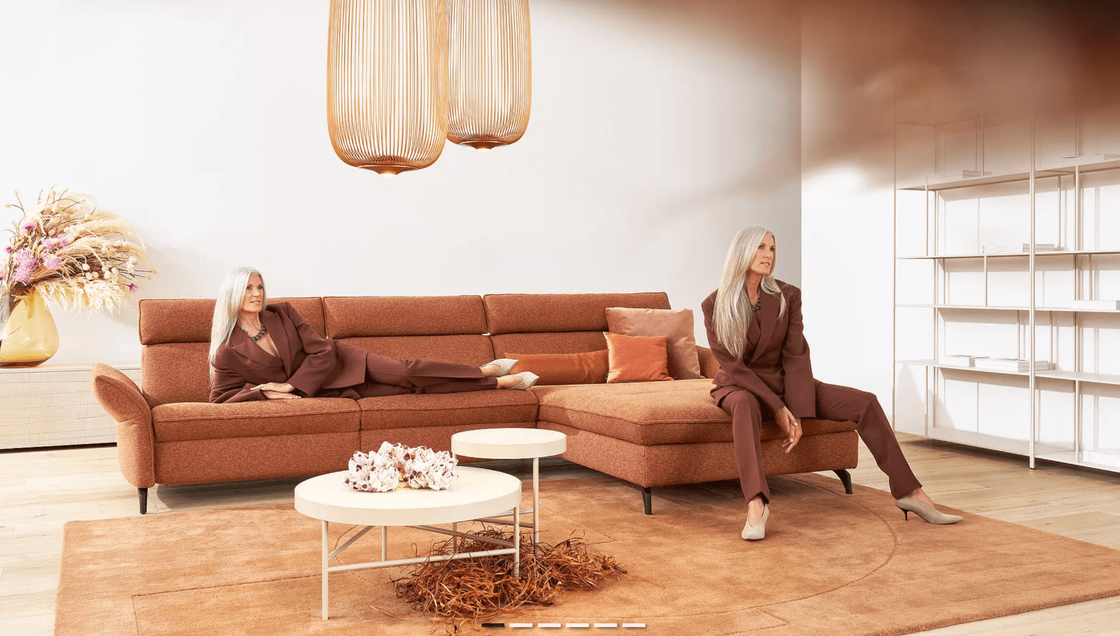 Minimalistisches Wohnzimmer mit Terrakotta-Sofa, warmen Erdtönen und zwei Frauen