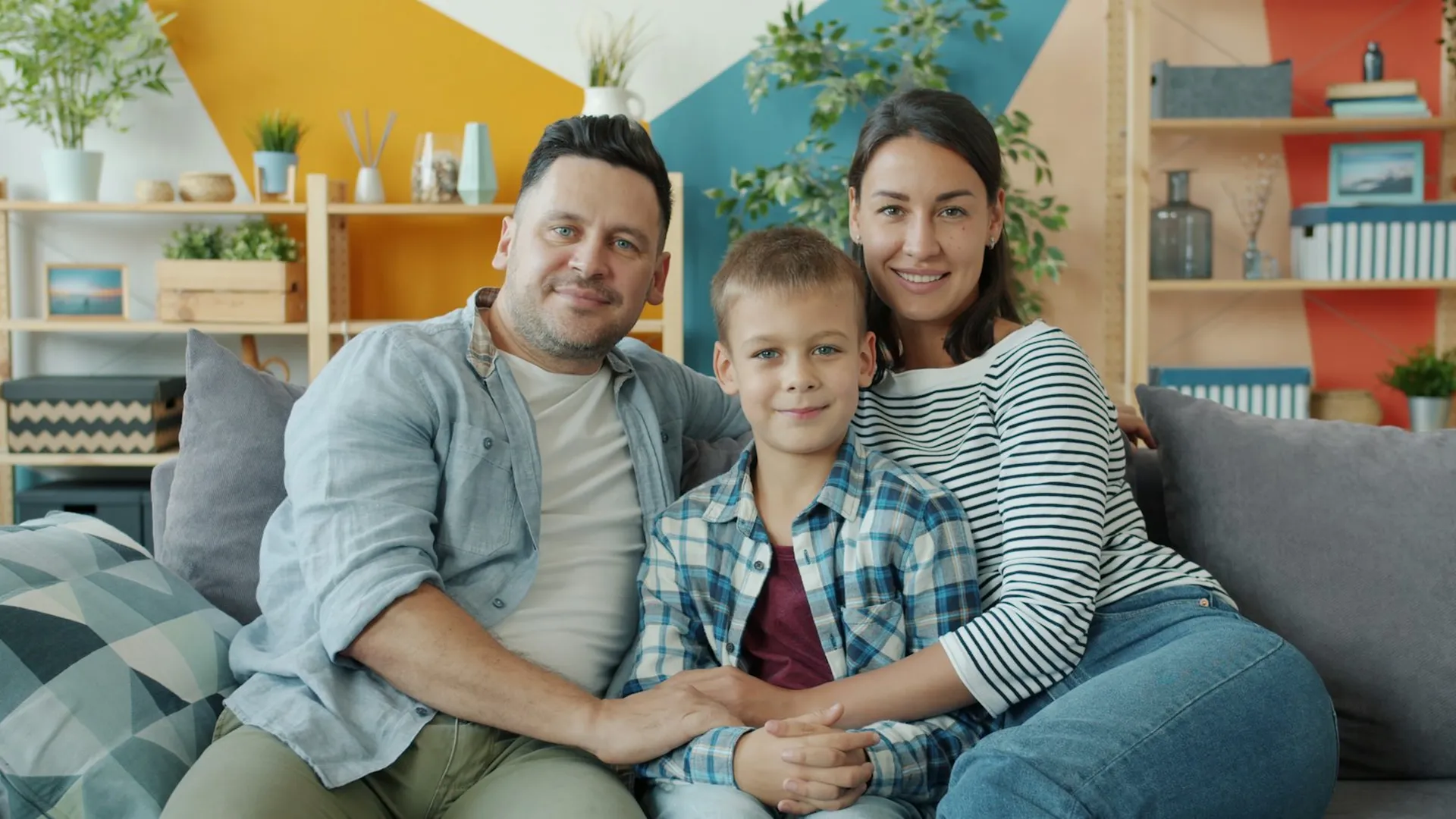 Familie mit Kind sitzt lachend gemeinsam auf dem Sofa