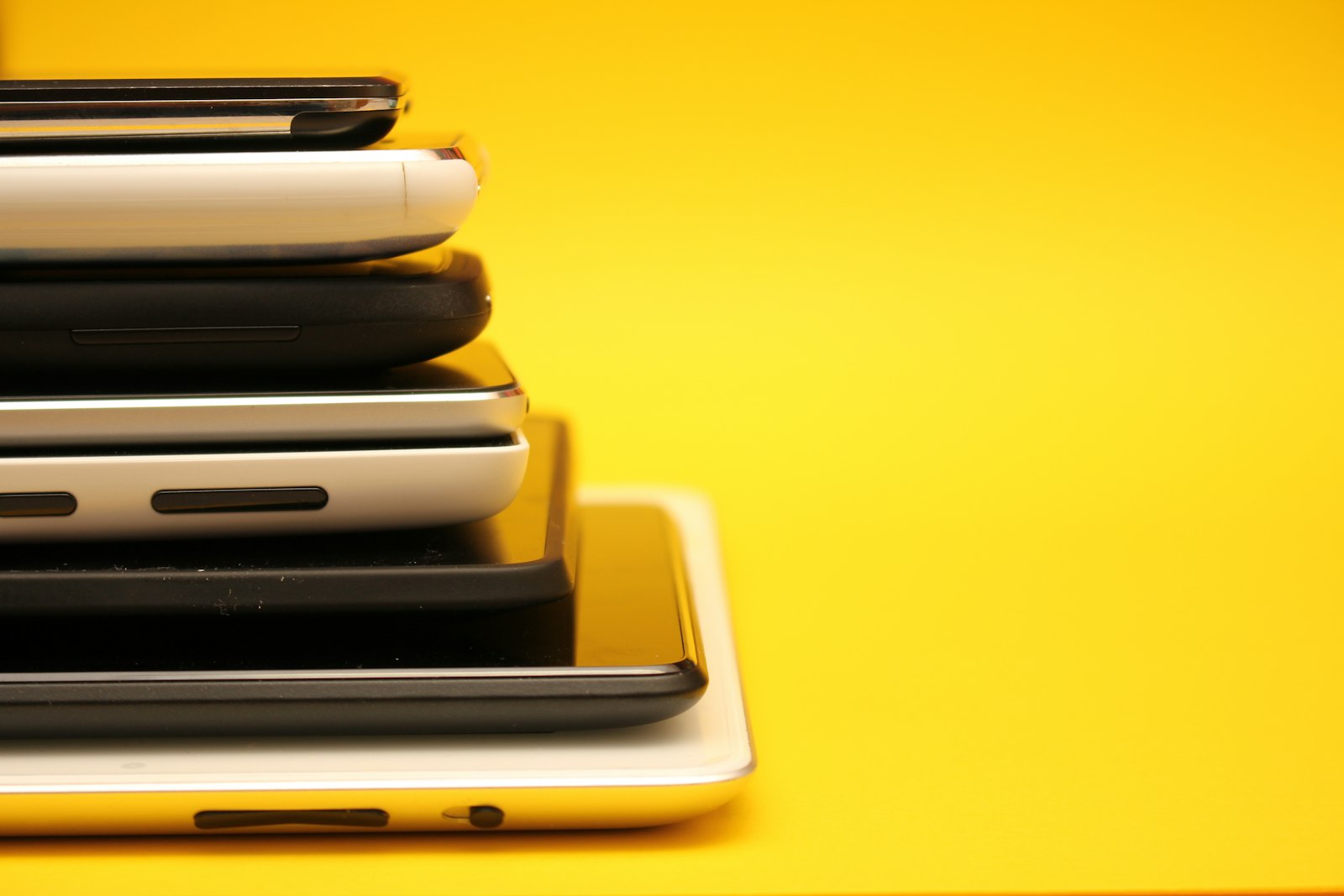 Gestapelte Smartphones und Tablets vor gelbem Hintergrund