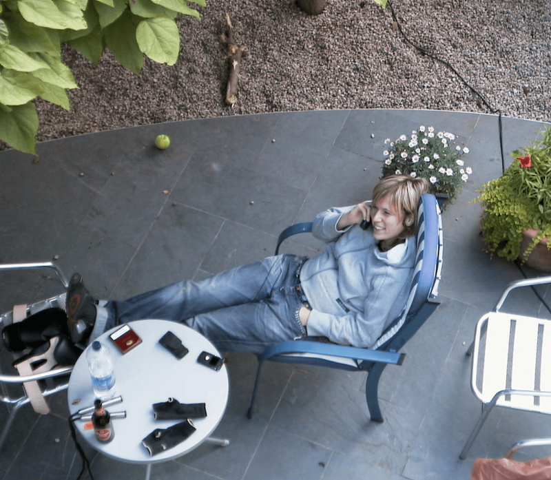 Entspannte Frau telefoniert im Liegestuhl auf ruhiger Terrasse mit Pflanzen