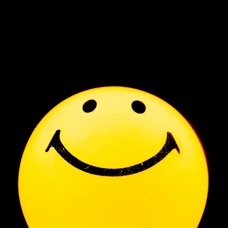 Leuchtender gelber Smiley vor schwarzem Hintergrund