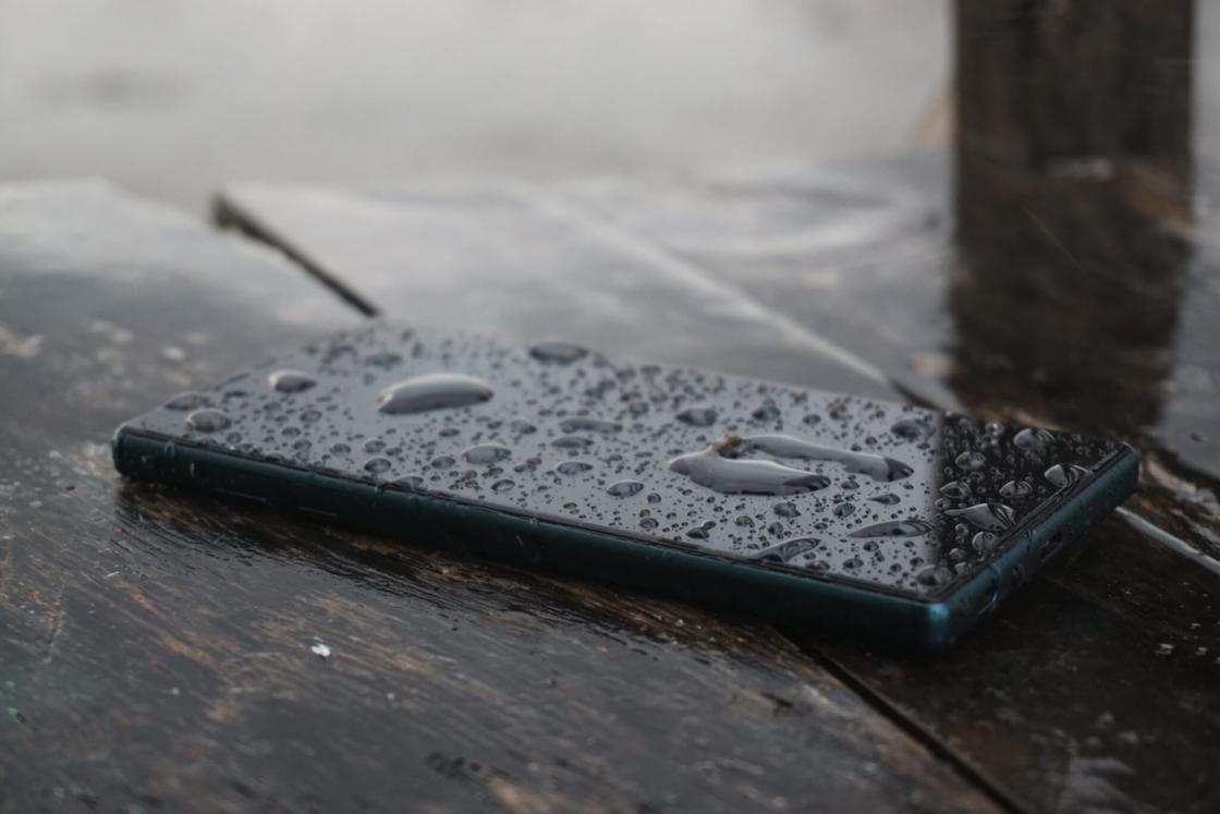 Nasses Smartphone mit Regentropfen auf Holz