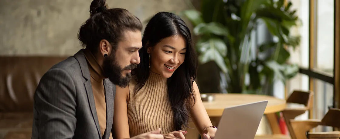 Zwei Kollegen arbeiten entspannt zusammen am Laptop in gemütlichem Café