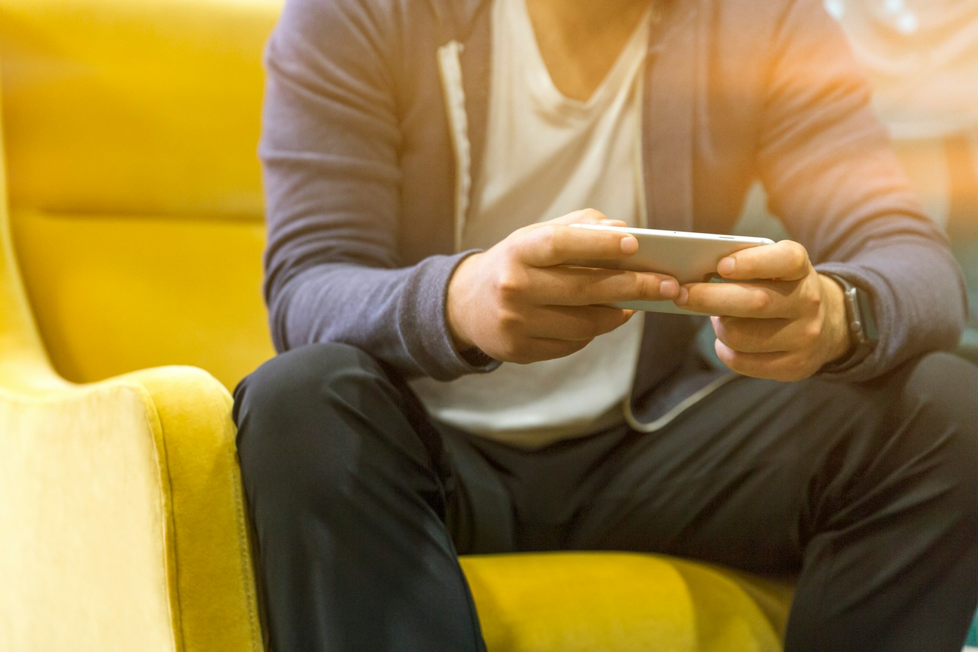 Person nutzt ein Smartphone auf einem gelben Sessel