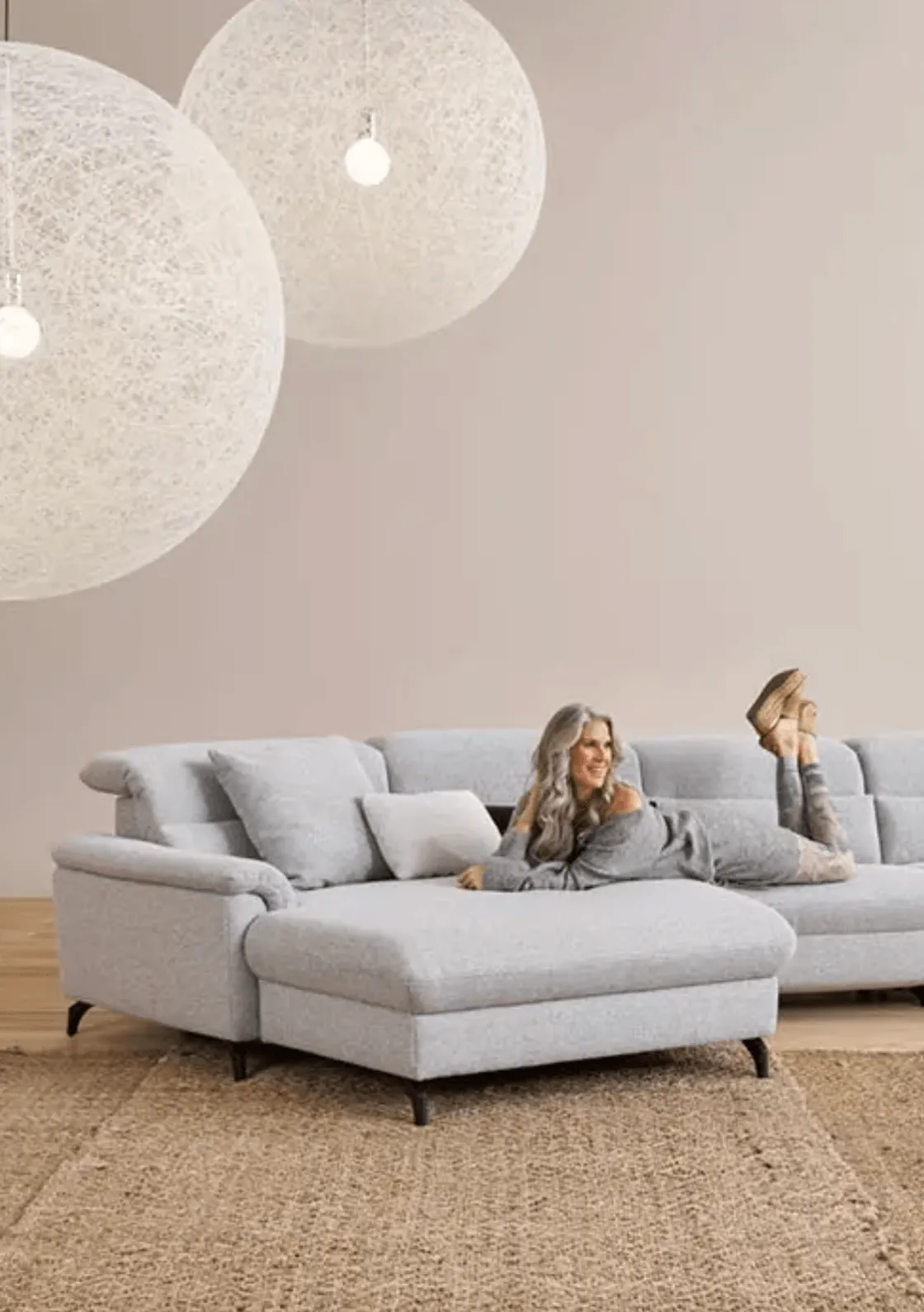 Modernes, minimalistisches Wohnzimmer mit grauem Ecksofa, Hängelampen und entspannter Person