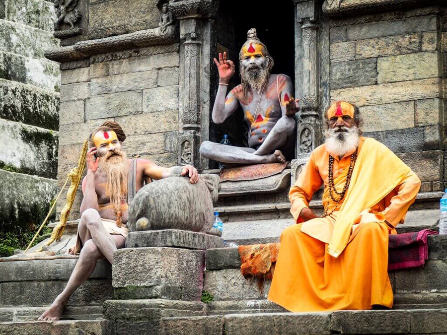 Drei Sadhus mit bunter Gesichtsbemalung auf verwitterten Stufen