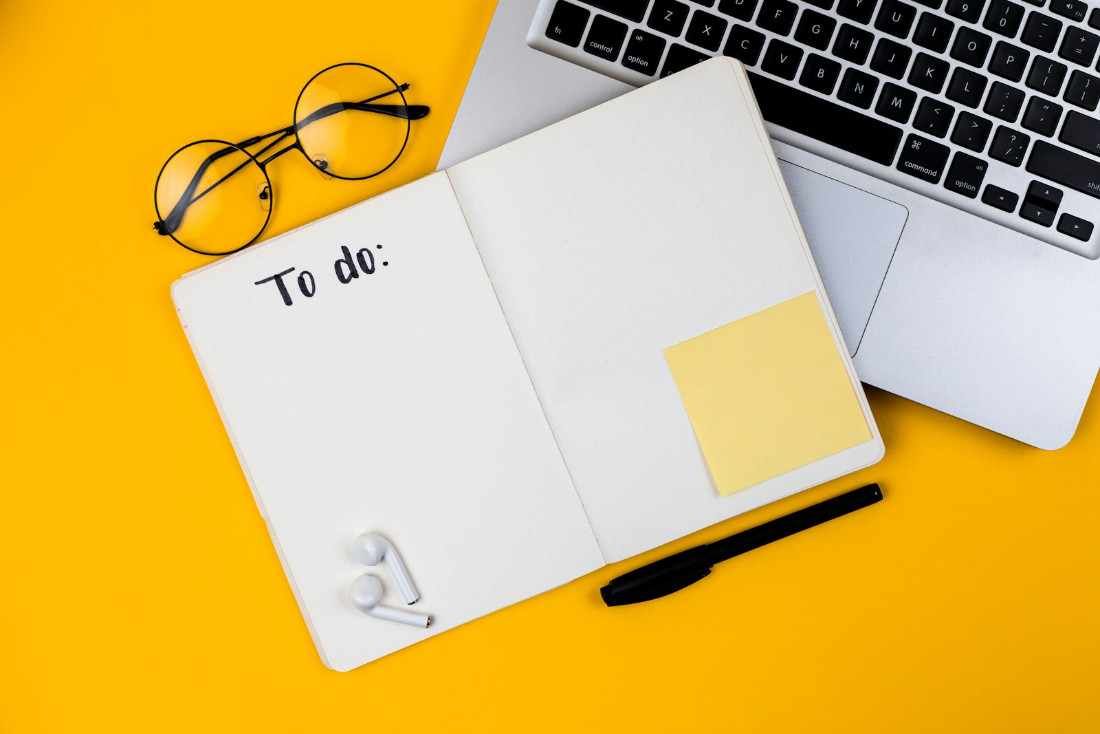 Notizbuch mit To-do-Liste neben Laptop auf gelbem Grund