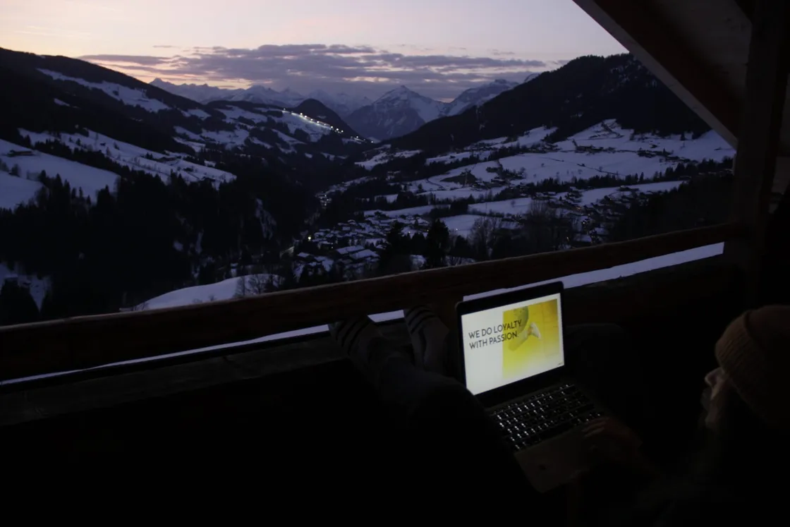 Laptop auf Balkon, Blick ins schneebedeckte Wintertal bei Dämmerung