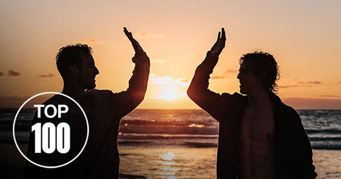 Zwei Männer geben sich bei Sonnenuntergang am Strand ein High Five, Top-100-Siegel