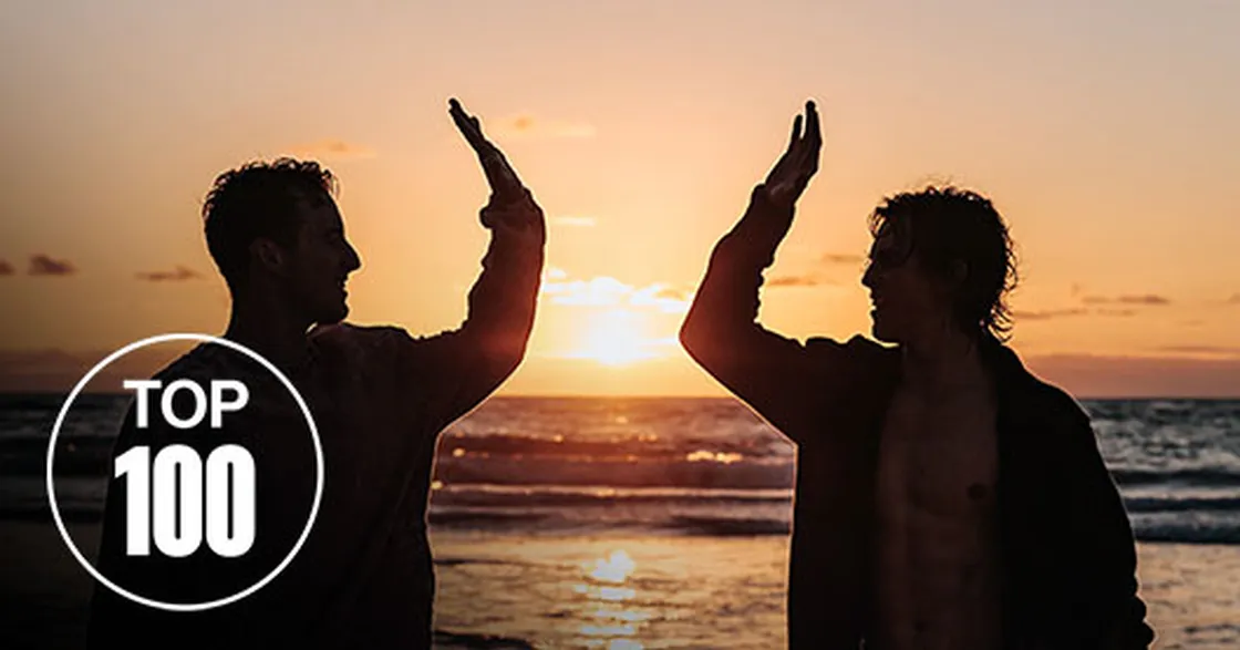 Zwei Männer geben sich bei Sonnenuntergang am Strand ein High Five, Top-100-Siegel