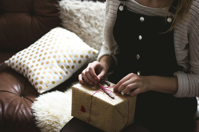 Frau öffnet auf dem Sofa ein gelbes Geschenk