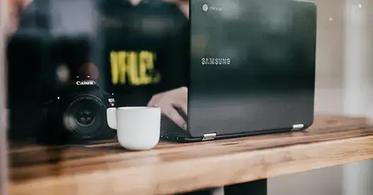 Minimalistischer Fotoarbeitsplatz: Kamera, Tasse und Laptop auf Holz
