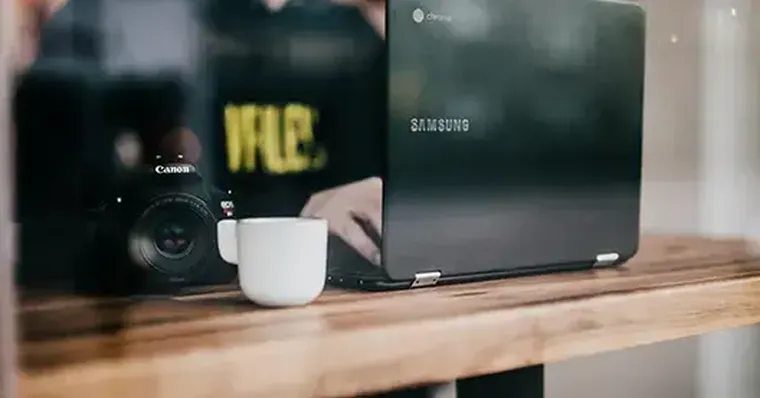 Minimalistischer Fotoarbeitsplatz: Kamera, Tasse und Laptop auf Holz