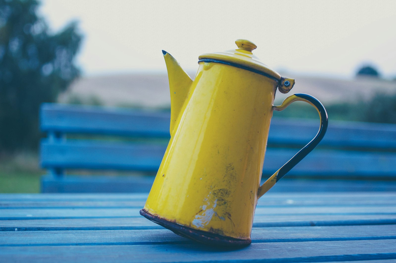 Gelbe Kaffeekanne auf einer blauen Holzbank