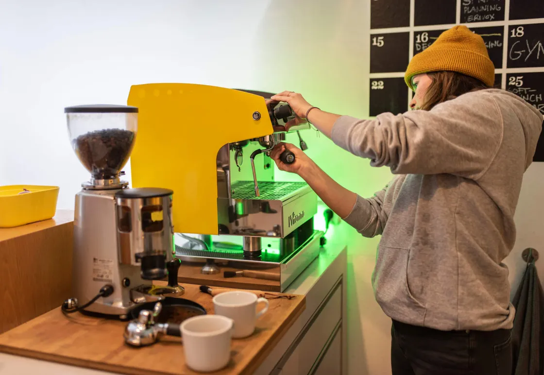 Barista setzt Siebträger in gelbe Espressomaschine neben Kaffeemühle für Espresso