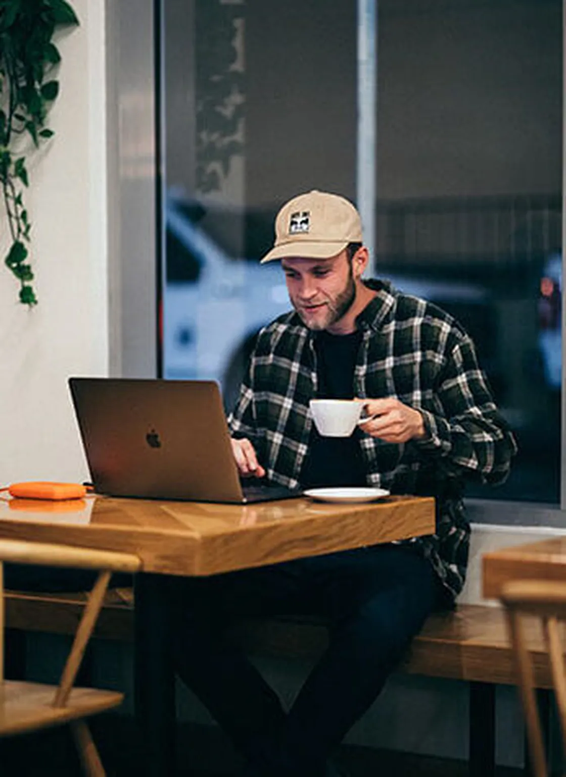 Mann mit Kappe trinkt Kaffee und arbeitet am Laptop im Café