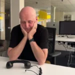 Nachdenklicher Mann im Büro am Schreibtisch mit Retro-Telefon und In-Ear-Kopfhörern