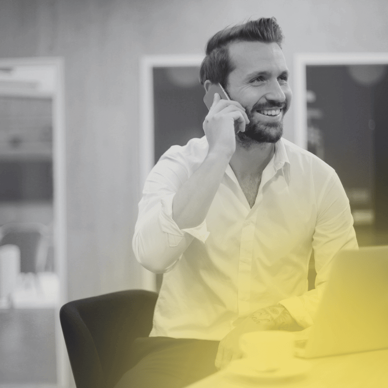 Mann im Büro telefoniert am Smartphone, Laptop offen – B2B-Loyalty-Programm.