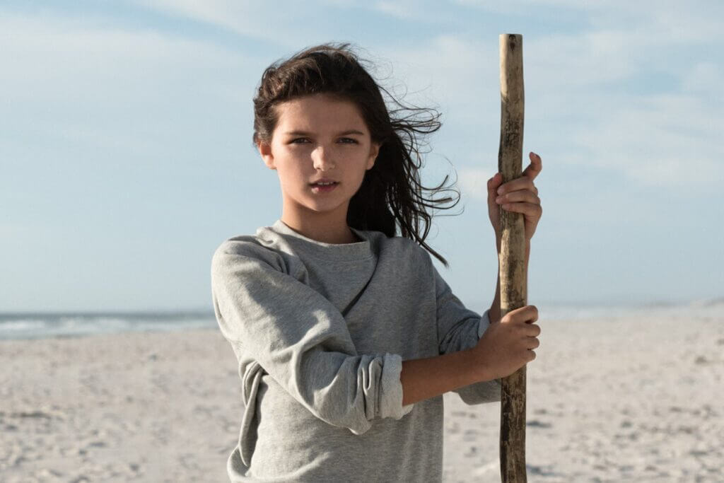 Jugendliche am weiten Strand mit Stock, direktem Blick und windgepeitschten Haaren