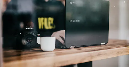 Minimalistischer Fotoarbeitsplatz: Kamera, Tasse und Laptop auf Holz