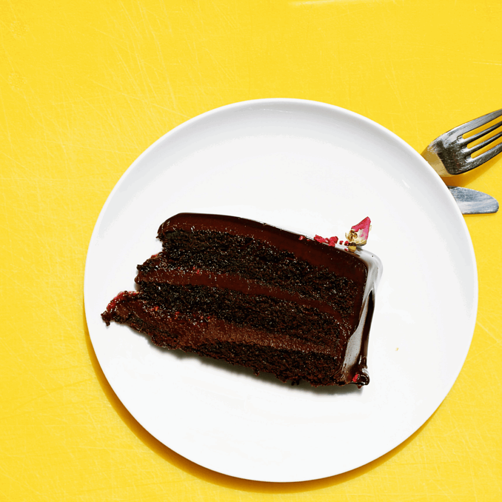 Glänzendes dreischichtiges Schokoladenkuchenstück auf weißem Teller vor gelbem Hintergrund