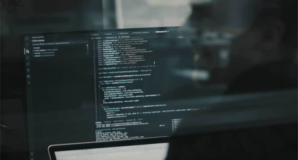 Monitor mit Quellcode, unscharfer Entwickler im Hintergrund – konzentriertes Programmieren im Büro