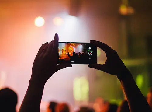 Konzertszene durch Smartphone-Bildschirm: Hände im Publikum, leuchtende Bühnenlichter