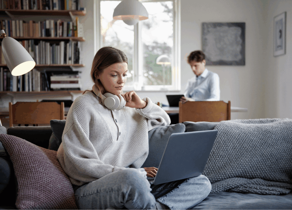Homeoffice: Sofa mit Laptop und Kopfhörern, zweite Person am Schreibtisch