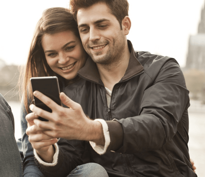 Lächelndes Paar teilt Smartphone für Selfie draußen in urbaner, gemütlicher Atmosphäre