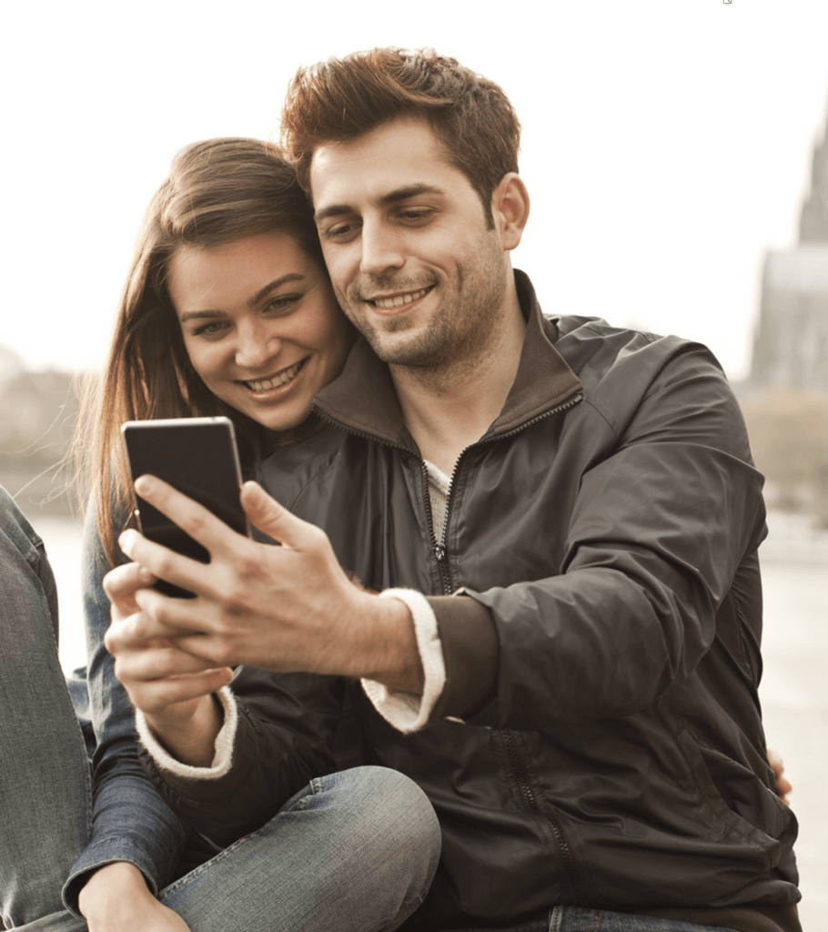 Lächelndes Paar teilt Smartphone für Selfie draußen in urbaner, gemütlicher Atmosphäre