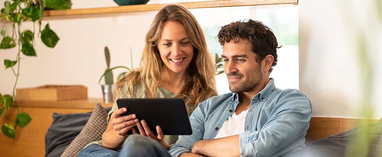Paar auf Couch im Wohnzimmer schaut gemeinsam Tablet