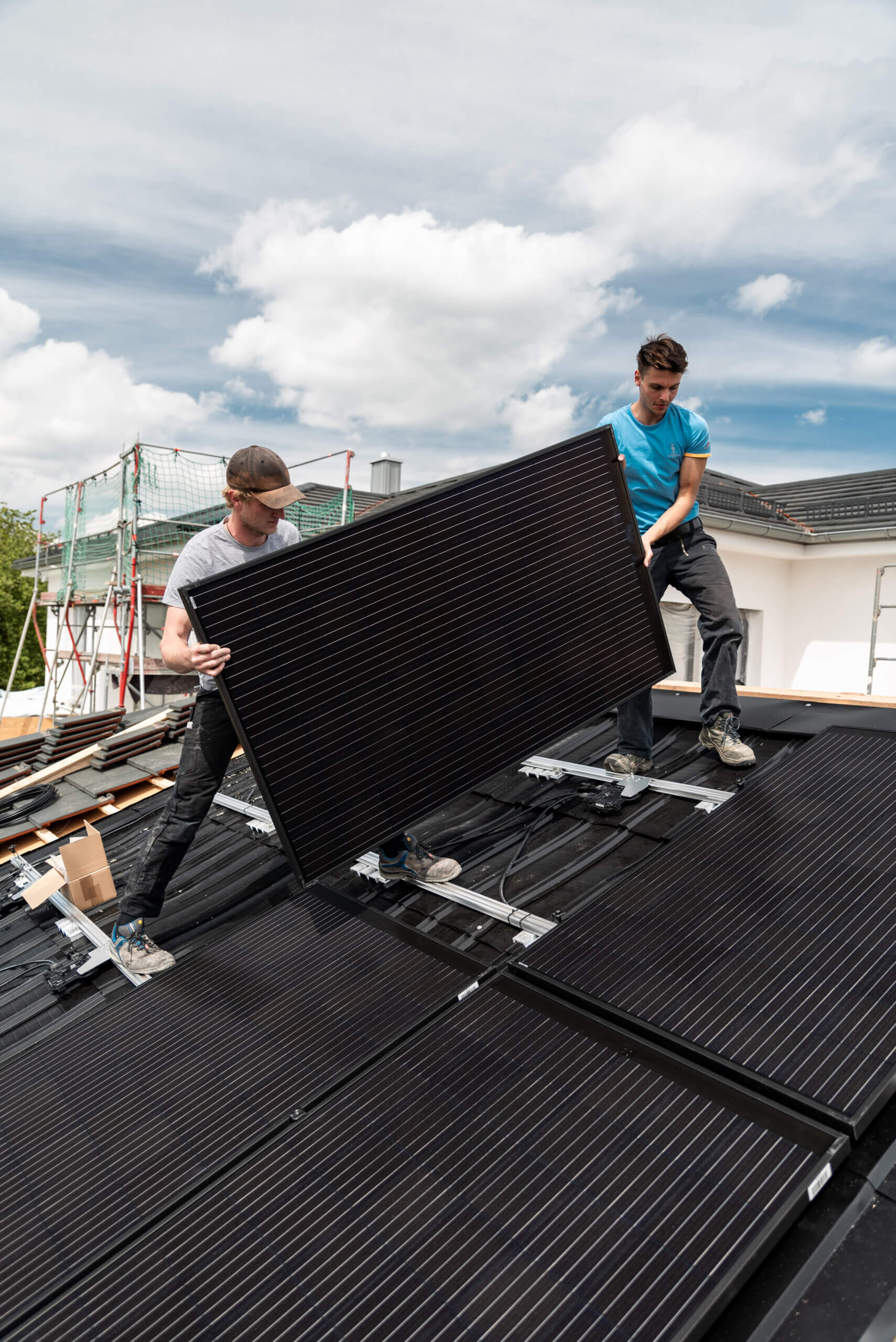 Partnerprogramm Photovoltaik für Verarbeiter: Zwei Handwerker montieren Solarmodul auf steilem Wohnhausdach