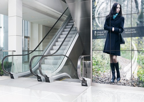 Moderne Rolltreppen im hellen Foyer neben großem Werbeplakat