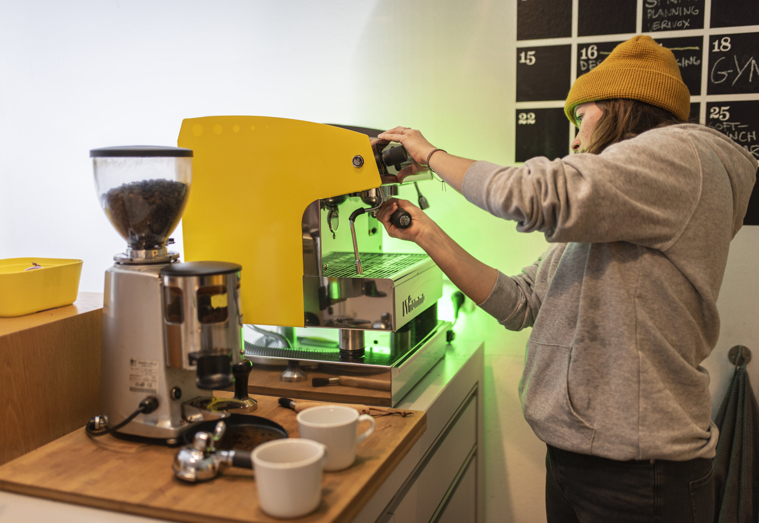 Barista setzt Siebträger in gelbe Espressomaschine neben Kaffeemühle für Espresso