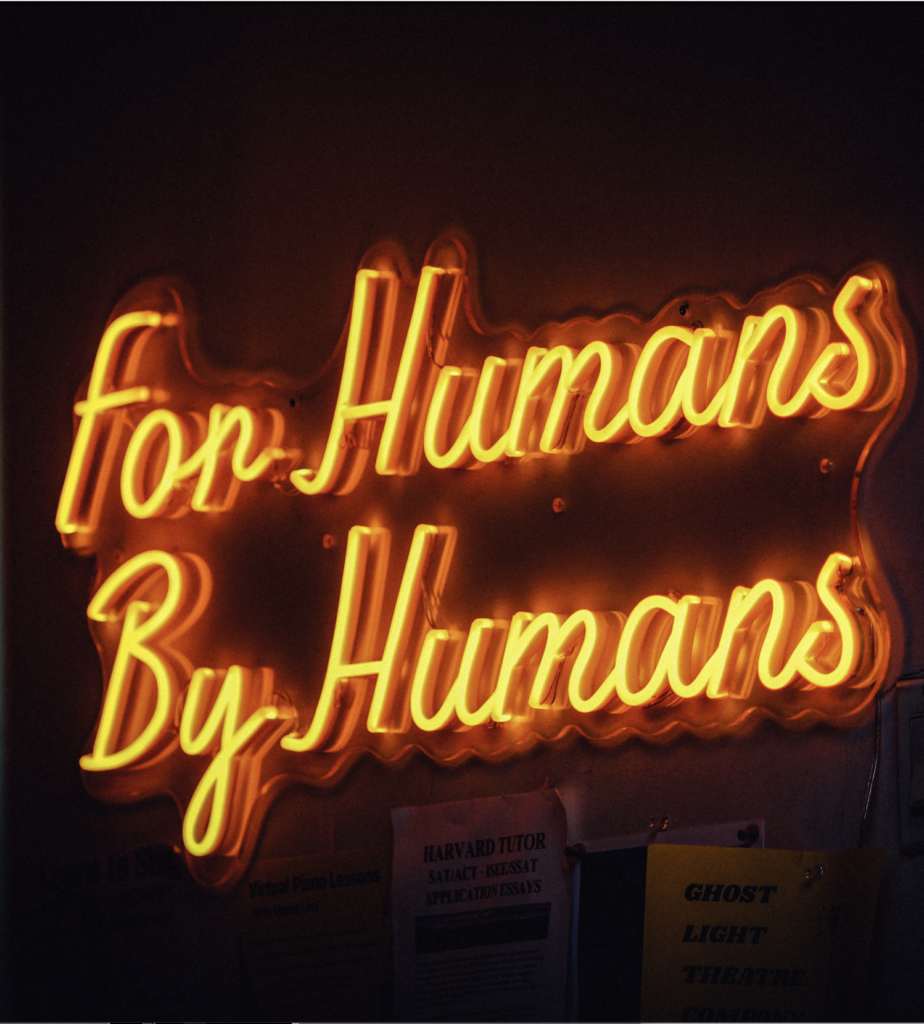 Warm leuchtendes Neon-Schild „For Humans By Humans“ über Posterwand mit Flyern