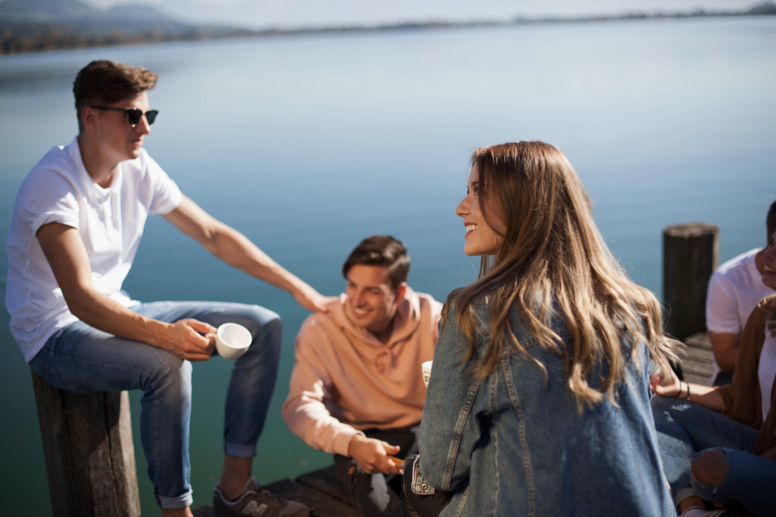 Kunden werben Kunden: Freunde lachen entspannt auf einem Holzsteg am See