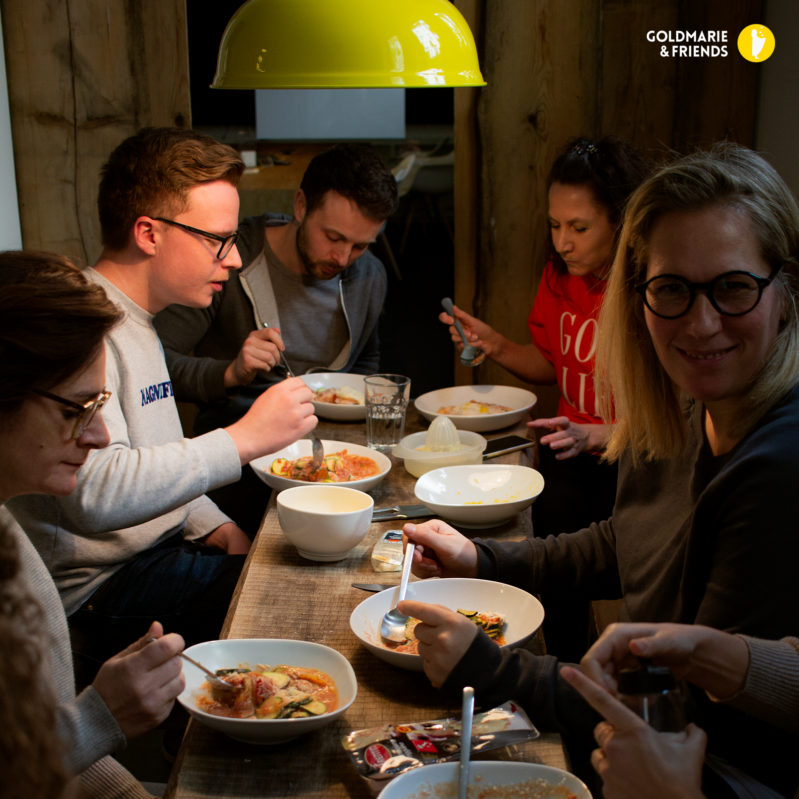 Gemütliches Abendessen mit Freunden am Holztisch unter warmer Hängelampe.