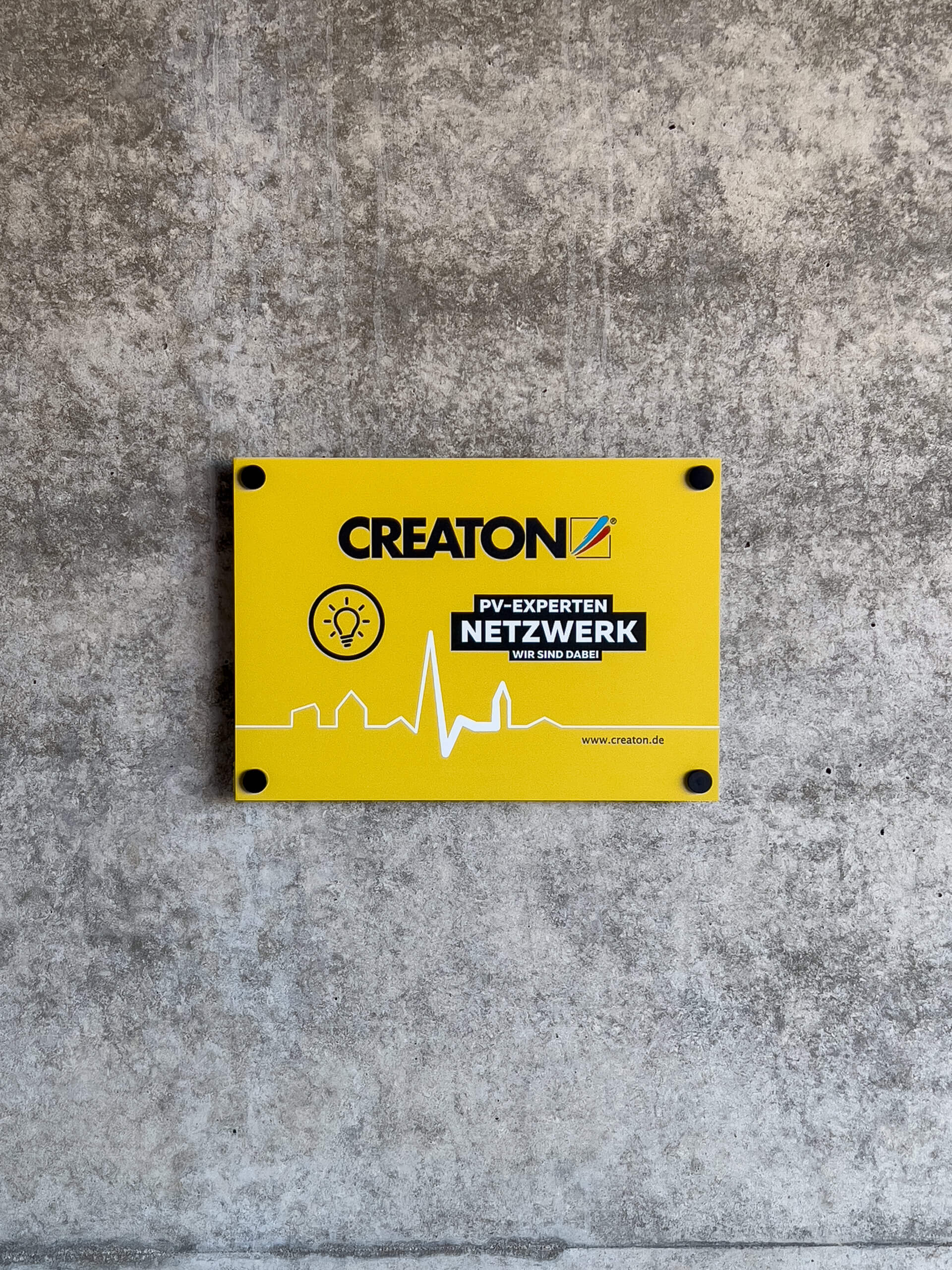 CREATON Partnerprogramm Photovoltaik für Verarbeiter – gelbes Schild an Betonwand