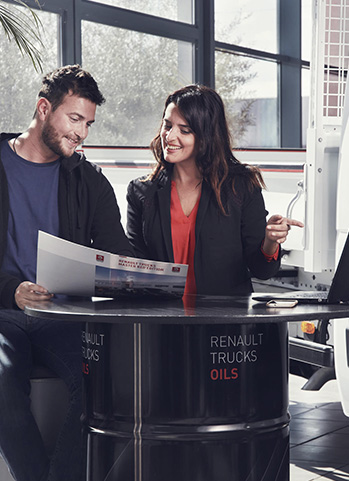 Industrielles Teammeeting mit Laptop und Dokumenten: zwei Personen besprechen Unterlagen in Werkstatt.