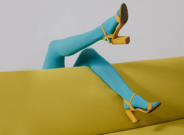 Türkise Strumpfhose und senfgelbe Sandalen auf gelbem Sofa, Beine gekreuzt.