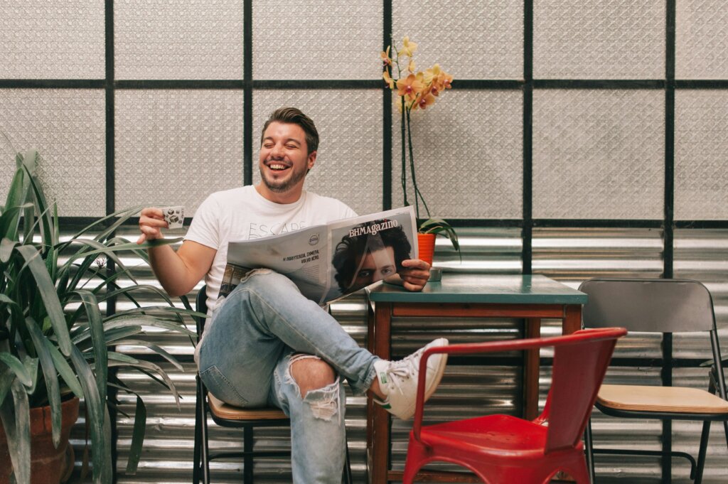 Lachender Mann im modernen Café mit Kaffee und Zeitung, entspannte Atmosphäre