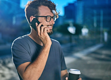 Lächelnder Mann telefoniert mit Handy und Kaffee in der Stadt