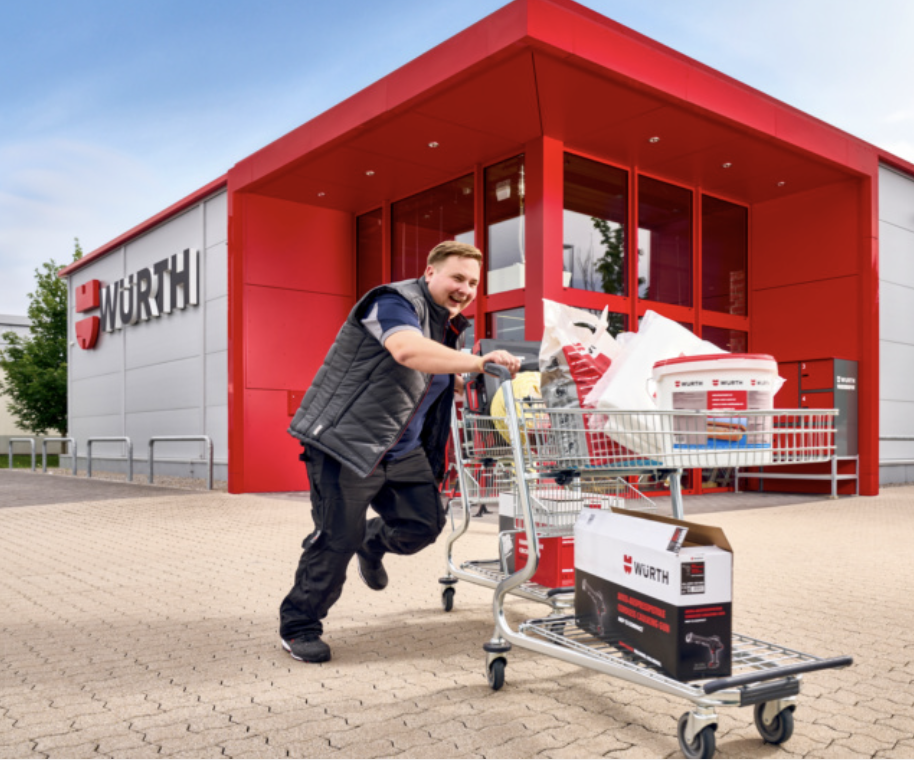 Punkteprogramm: Mitarbeiter schiebt volle Einkaufswagen vor der roten Filiale.