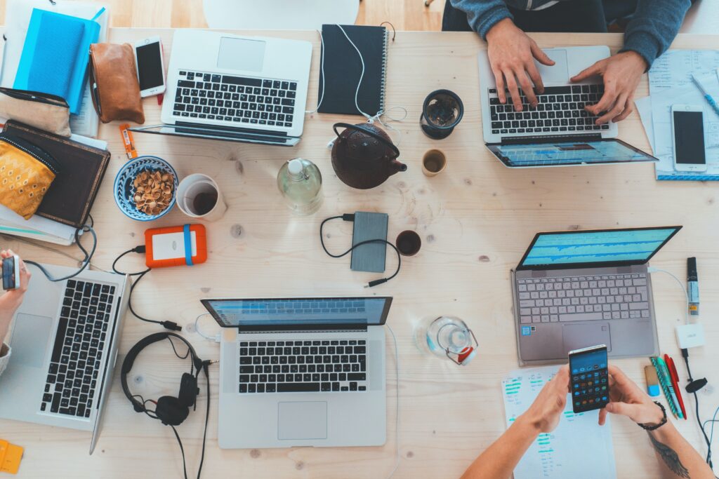 Ein lächelnder Mann sitzt an einem Tisch mit einer Tasse Kaffee und einem Laptop, umgeben von Pflanzen