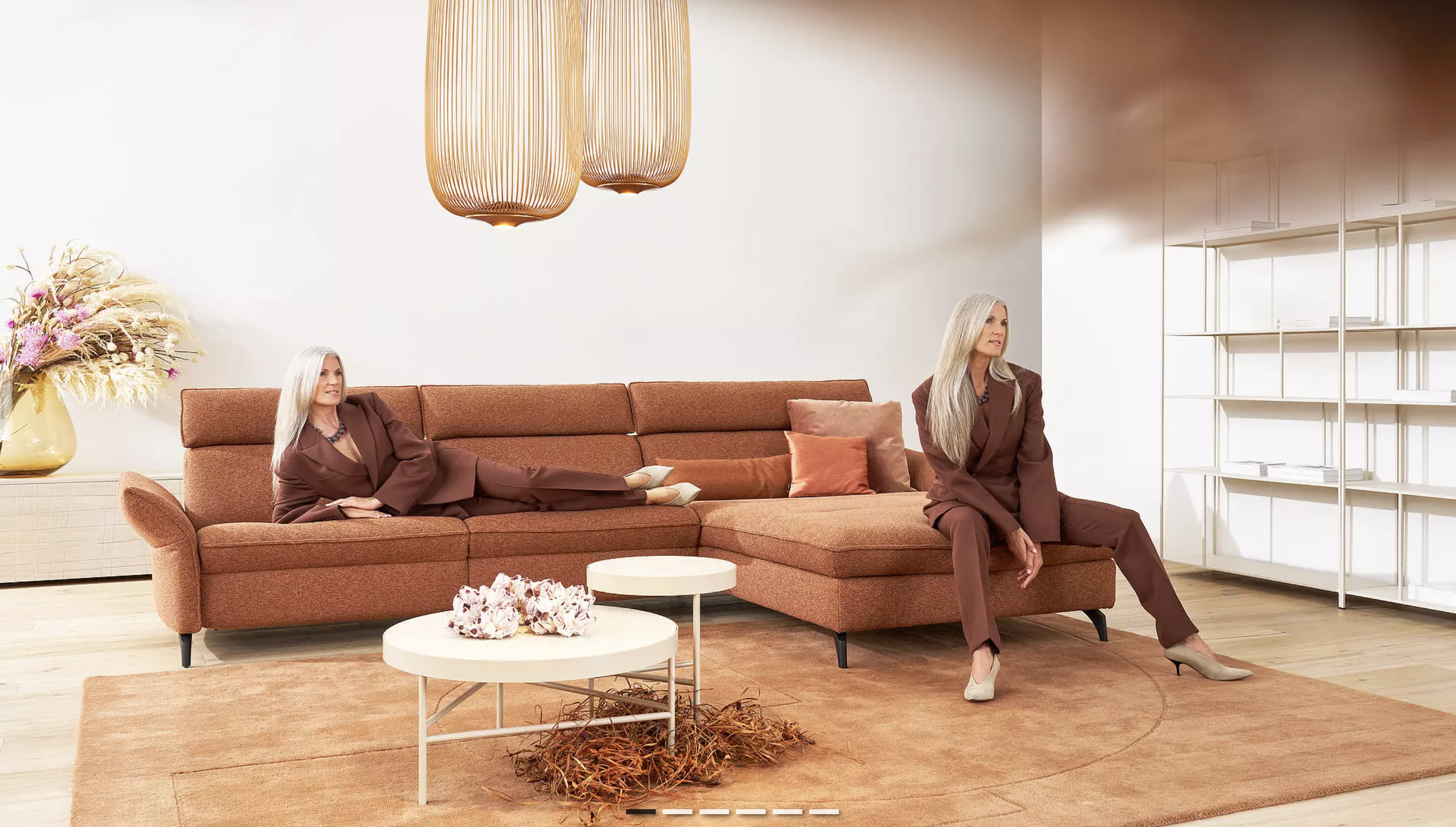 Minimalistisches Wohnzimmer mit Terrakotta-Sofa, warmen Erdtönen und zwei Frauen